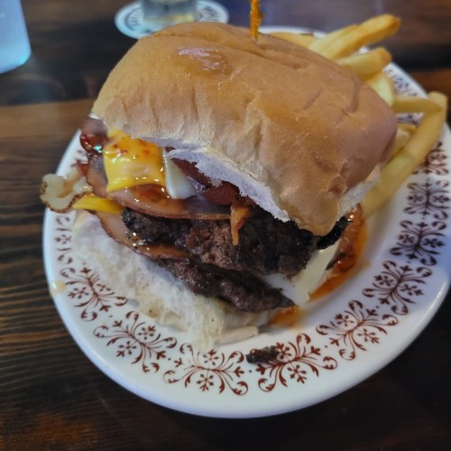 A juicy burger with bacon, cheese, and sauce, served with a side of golden fries on a decorative plate.