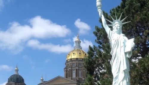 Statue of Liberty replica in front of a golden-domed building under a blue sky with clouds.