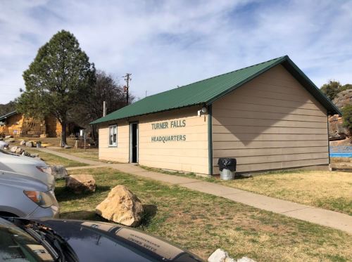 A single-story building with a green roof labeled "Turner Falls Headquarters," surrounded by grass and rocks.