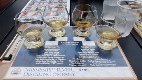 Four whiskey tasting glasses on a tasting flight sheet at Mississippi River Distilling Company, with various selections listed.