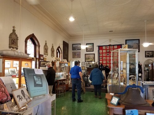 Visitors explore a museum filled with historical exhibits, photographs, and artifacts in a well-lit room.