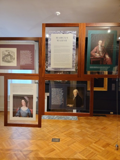 A display of framed artworks and information panels about Marcus Marsh in a museum setting.