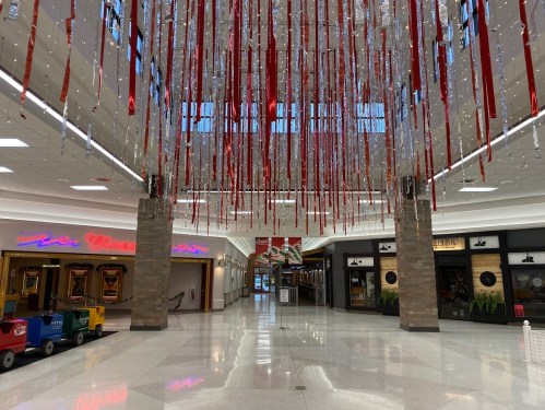 A spacious mall interior with red and silver streamers hanging from the ceiling, featuring closed storefronts and a train ride.