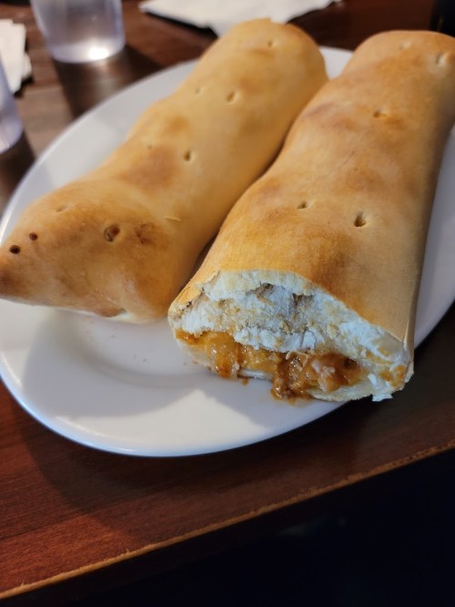 Two golden-brown calzones on a white plate, one cut open to reveal a savory filling.