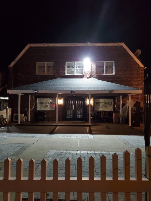 A brick building at night with a sign reading "Butchers," featuring a porch and outdoor seating area.