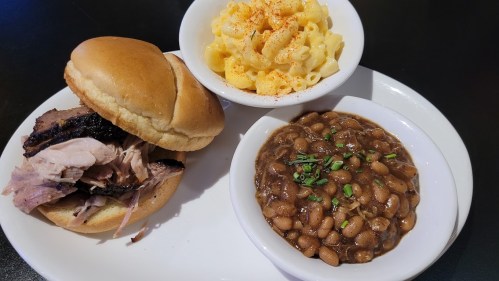 A plate featuring a pulled pork sandwich, macaroni and cheese, and baked beans.