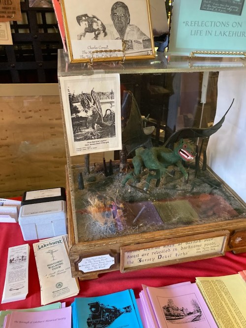 A display case featuring a model of the Jersey Devil, photos, and brochures about Lakehurst's history.