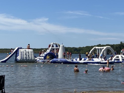 A crowded inflatable water park with people playing and swimming in a lake on a sunny day.
