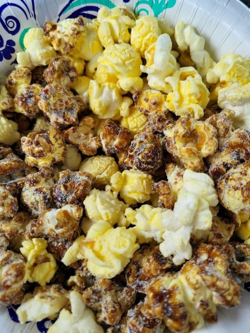 A colorful bowl of popcorn featuring a mix of caramel, cheese, and butter-flavored varieties.