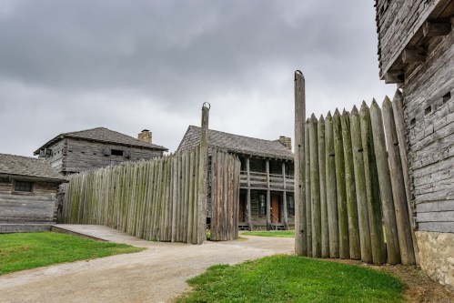 Historic wooden fort with a palisade, surrounded by grassy areas and overcast skies.