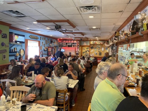 A busy diner filled with people dining and chatting, featuring colorful decor and a lively atmosphere.