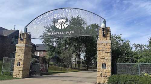 Entrance gate to Dubuque Arboretum and Botanical Gardens at Marshall Park, surrounded by trees and a clear blue sky.