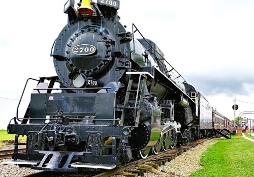 A vintage steam locomotive, numbered 2700, stands on the tracks with a cloudy sky in the background.