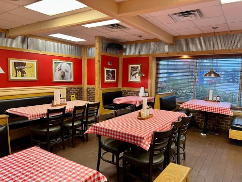 Cozy restaurant interior with red walls, checkered tablecloths, and framed animal photos. Warm, inviting atmosphere.