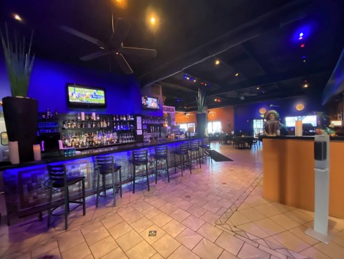 A vibrant bar interior with colorful lighting, a long bar counter, and TVs displaying sports in a lively atmosphere.