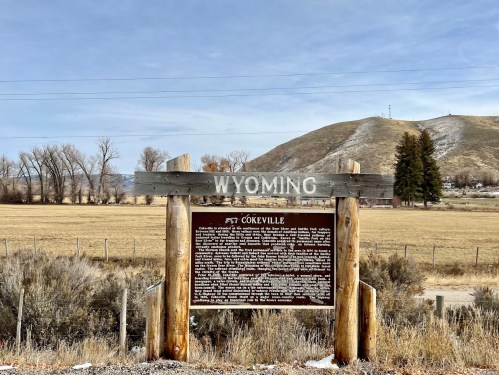 Sign marking the entrance to Cokeville, Wyoming, with a grassy field and hills in the background.