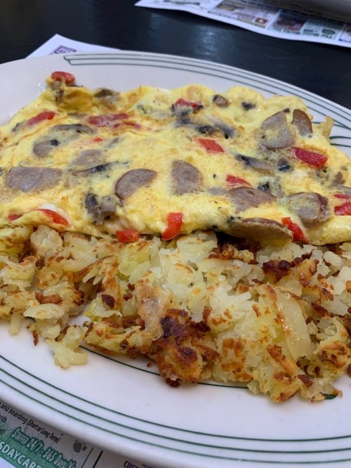 A plate of a vegetable omelette with mushrooms and red peppers, served with crispy golden hash browns.