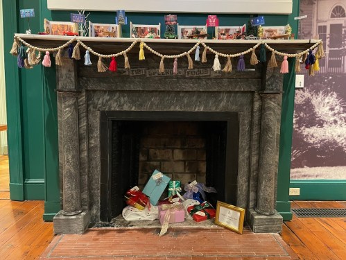 A decorated fireplace with a garland, photos on the mantel, and colorful wrapped gifts at the base.