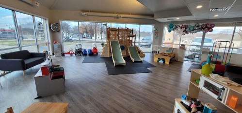 Bright playroom with slides, toys, and a cozy seating area, featuring large windows and a playful atmosphere.