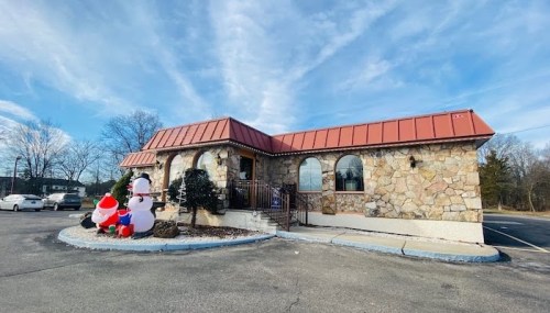 A stone building with a red roof, featuring holiday decorations, including snowmen and Santa, in a parking lot.