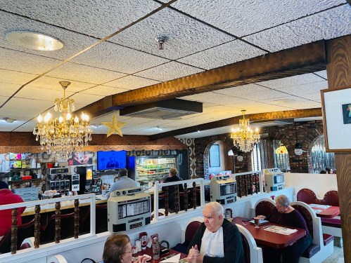 A cozy diner interior with vintage decor, chandeliers, and patrons enjoying their meals at booths.