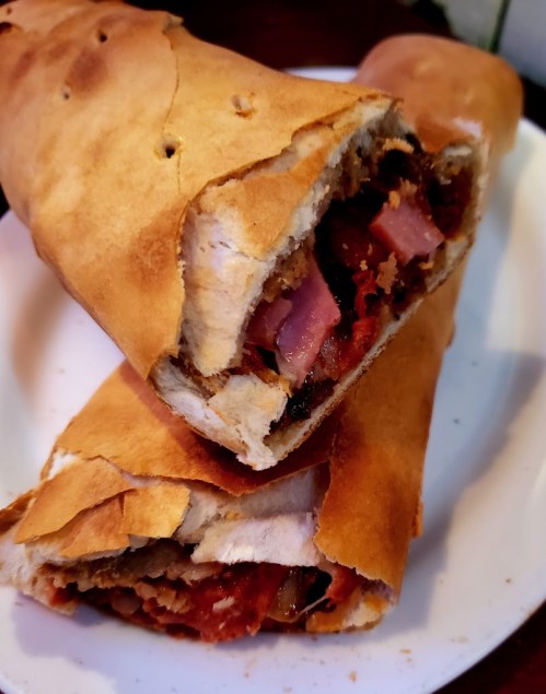 Two slices of a golden-brown calzone filled with meat and cheese, resting on a white plate.
