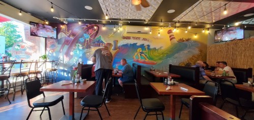 A vibrant restaurant interior with a colorful mural, string lights, and patrons enjoying their meals at wooden tables.