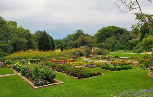 A vibrant garden filled with colorful flowers and neatly arranged flower beds, surrounded by lush greenery under a cloudy sky.