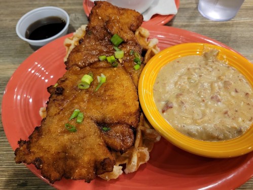 A plate featuring fried fish on waffles, topped with green onions, alongside a bowl of creamy seafood chowder.
