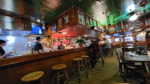A cozy restaurant interior with wooden decor, bar stools, and patrons enjoying their meals. Holiday decorations are visible.