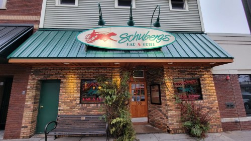Exterior of Schwerg's Bar & Grill, featuring a green awning, brick facade, and decorative plants by the entrance.