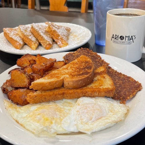 A plate of breakfast with eggs, toast, hash browns, and potatoes, alongside a plate of French toast and a coffee cup.