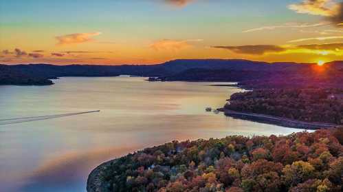 A serene lake at sunset, surrounded by colorful autumn foliage and rolling hills under a vibrant sky.