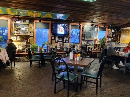 Cozy restaurant interior with wooden decor, tables, and a TV, featuring patrons enjoying their meals.