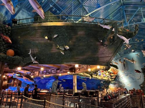 A large, decorated boat hangs from the ceiling in an aquarium-themed restaurant, surrounded by marine life decor.