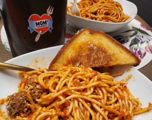 A bowl of spaghetti with meatballs and garlic bread, alongside a drink in a cup labeled "Mom's Spaghetti."