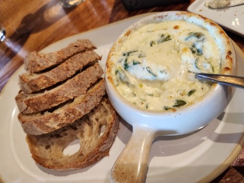 A bowl of creamy spinach dip served with slices of toasted bread on a plate.