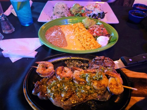 A sizzling plate of steak and shrimp with rice, beans, and guacamole, alongside a colorful plate of rice and salad.