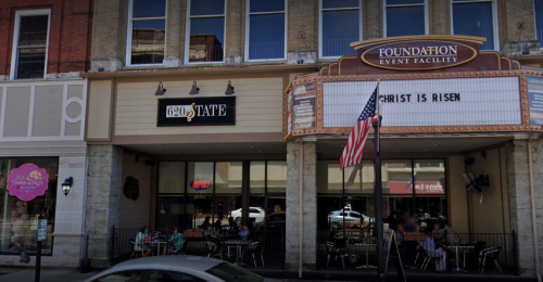 Exterior view of a building with a marquee reading "CHRIST IS RISEN" and a restaurant sign for "620 State." American flag visible.