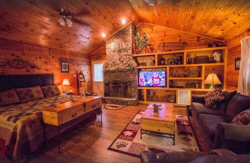 Cozy cabin interior with wooden walls, a stone fireplace, a TV, and rustic furniture, creating a warm atmosphere.