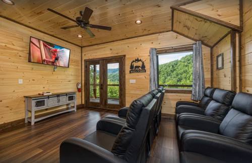 Cozy wooden room with leather recliners, a TV, and large windows showcasing a scenic mountain view.