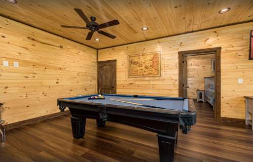 A cozy game room featuring a blue pool table, wooden walls, and a ceiling fan.