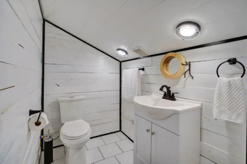 A small, modern bathroom with white walls, a toilet, sink, and stylish lighting.