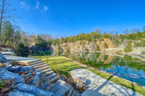 A serene landscape featuring a calm lake surrounded by rocky cliffs and trees under a clear blue sky.