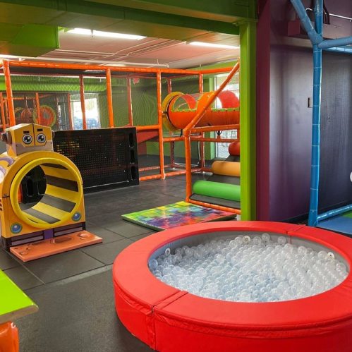 Colorful indoor play area featuring slides, tunnels, and a ball pit. Brightly colored structures and soft flooring.