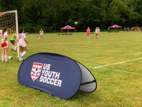A soccer field with players practicing, featuring a US Youth Soccer banner in the foreground.