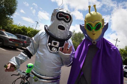 Two people in elaborate costumes: one in a silver robot suit and the other in an alien outfit with a purple cape.