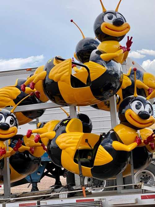 Colorful bee-shaped ride vehicles stacked on a trailer, featuring black and yellow designs with cheerful expressions.