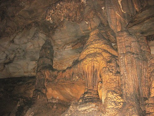Stalactites and stalagmites in a dimly lit cave, showcasing intricate rock formations and textures.