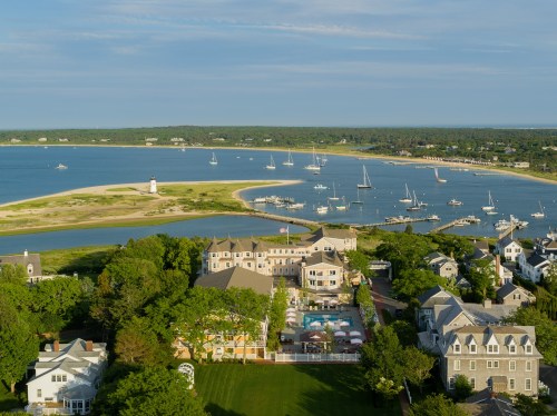 Aerial view of a coastal area with boats, a lighthouse, and a resort surrounded by greenery and water.